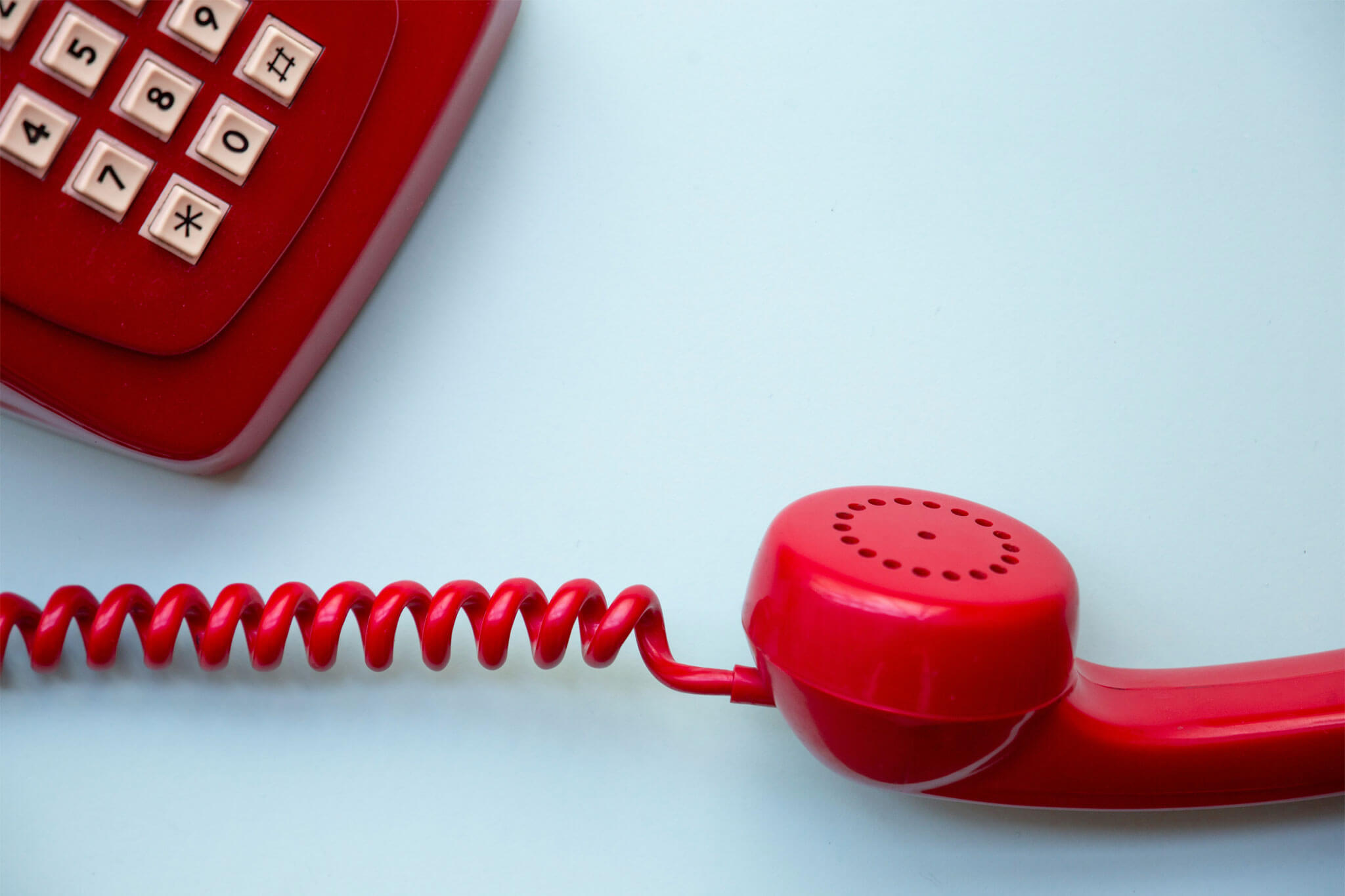 Red push button analogue telephone off the hook on blue background